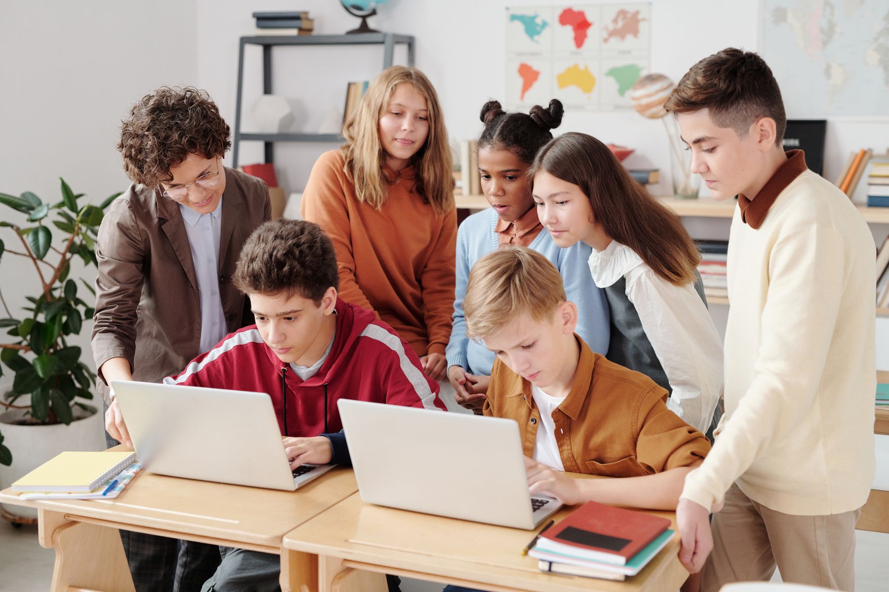 A diverse group of middle-school students collaborating on laptops with an educator.