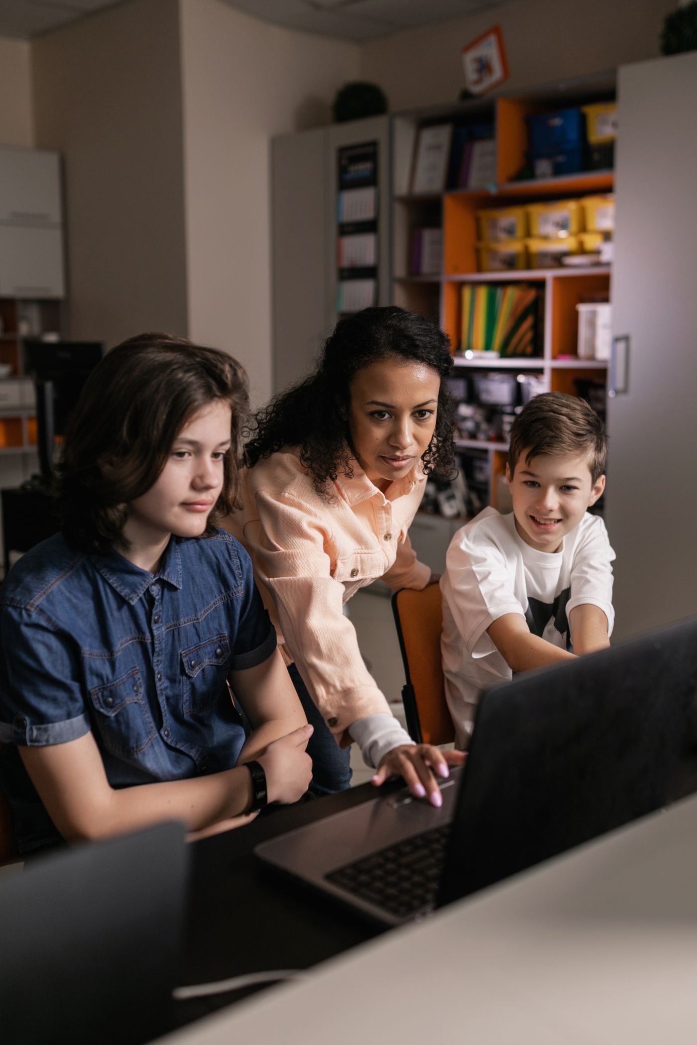 An educator and two students working together at a classroom computer.